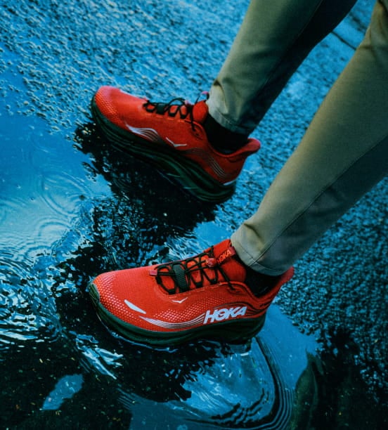Gros plan d’une personne debout dans l’eau boueuse en chaussures HOKA.
